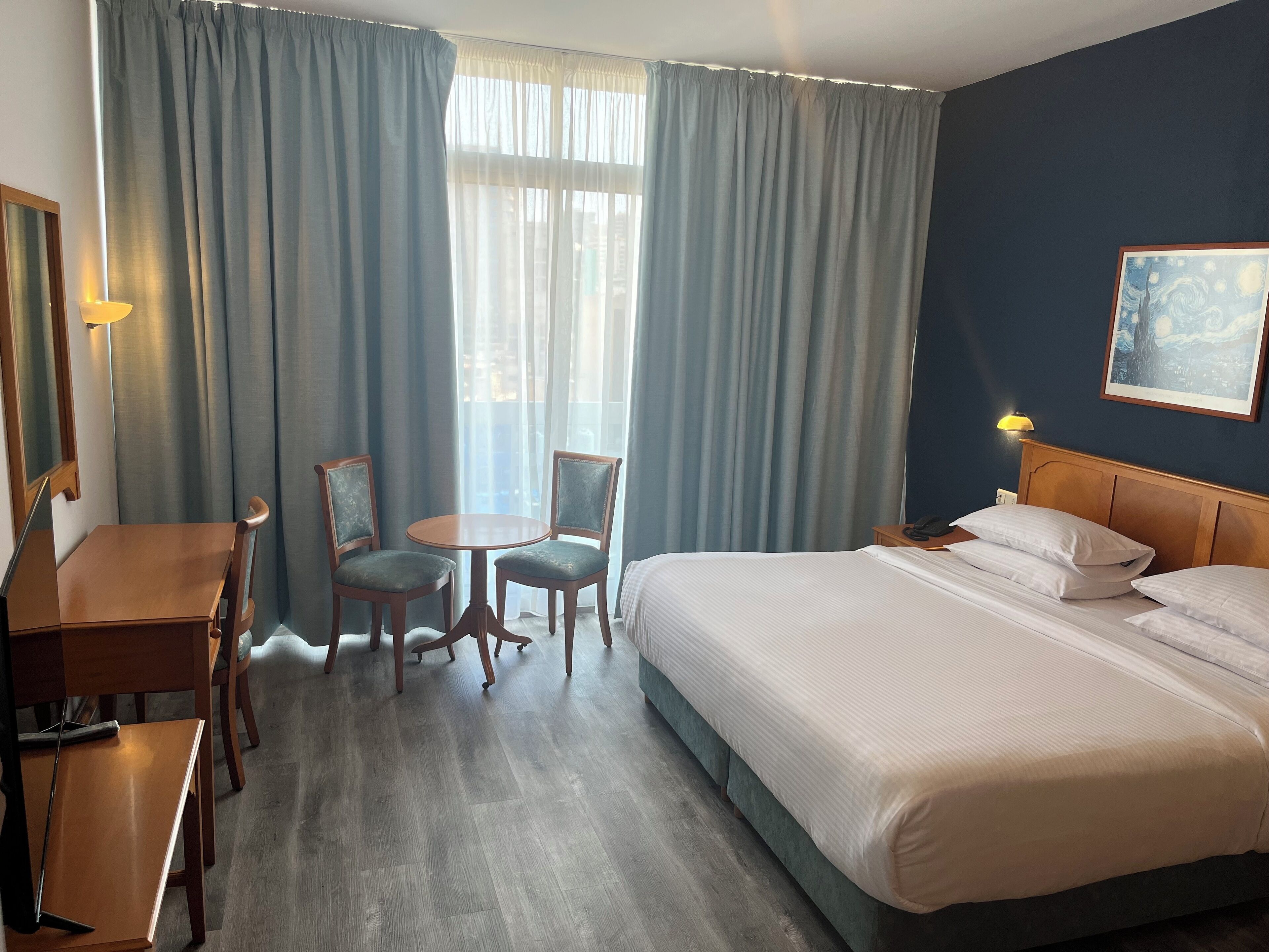 Een hotelkamer met een bed, twee stoelen, een tafeltje, een bureau en een lamp.