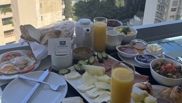 A breakfast spread on a balcony overlooking the sea, including eggs, toast, fruit, and beverages. - El Sheikh Suites Hotel (Beirut)