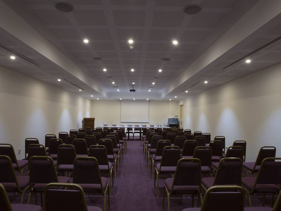 Un salón de conferencias con filas de sillas, una pantalla para proyector y un atril.