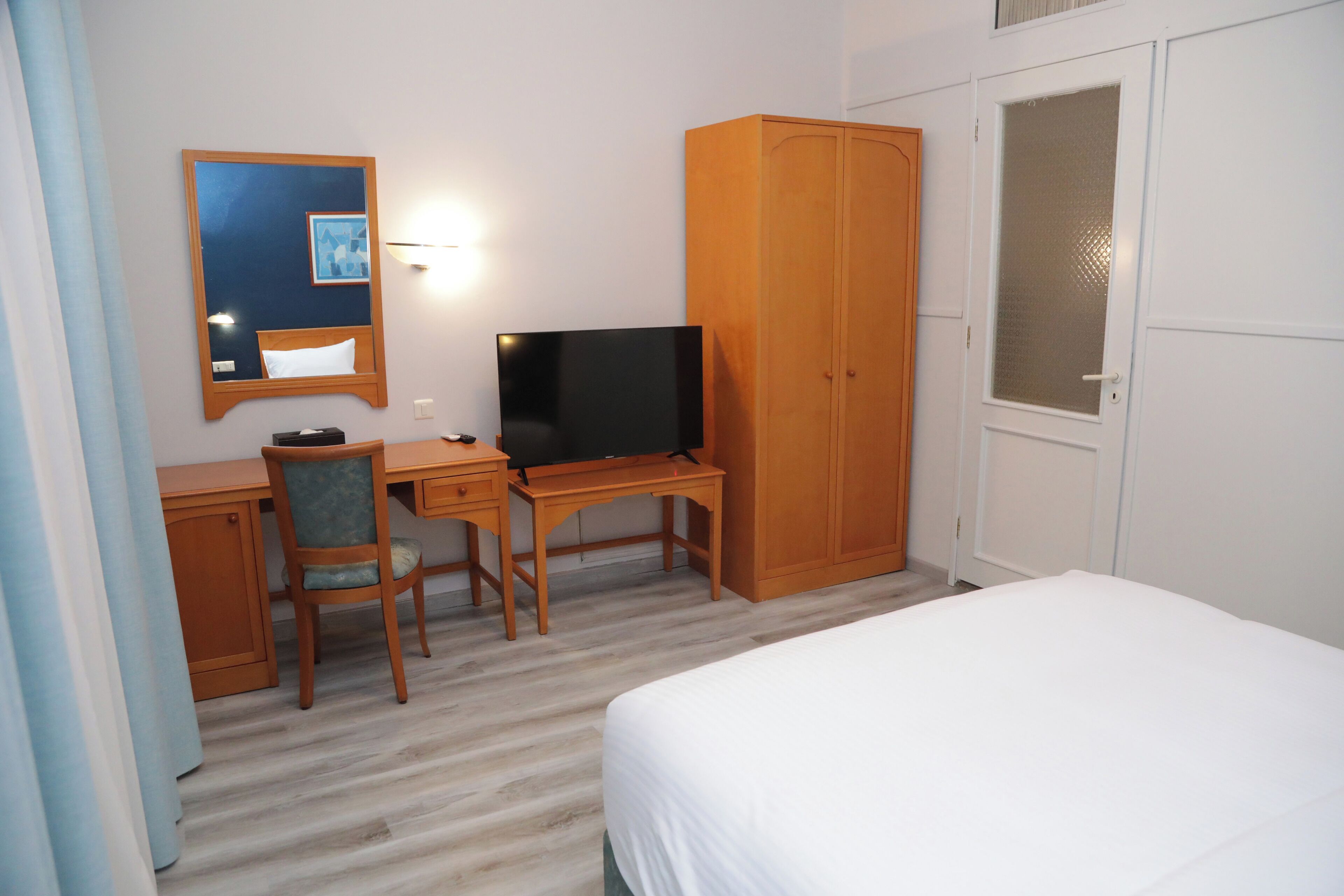 Una camera d'albergo con un letto, una scrivania con computer e sedia, una televisione e un armadio.