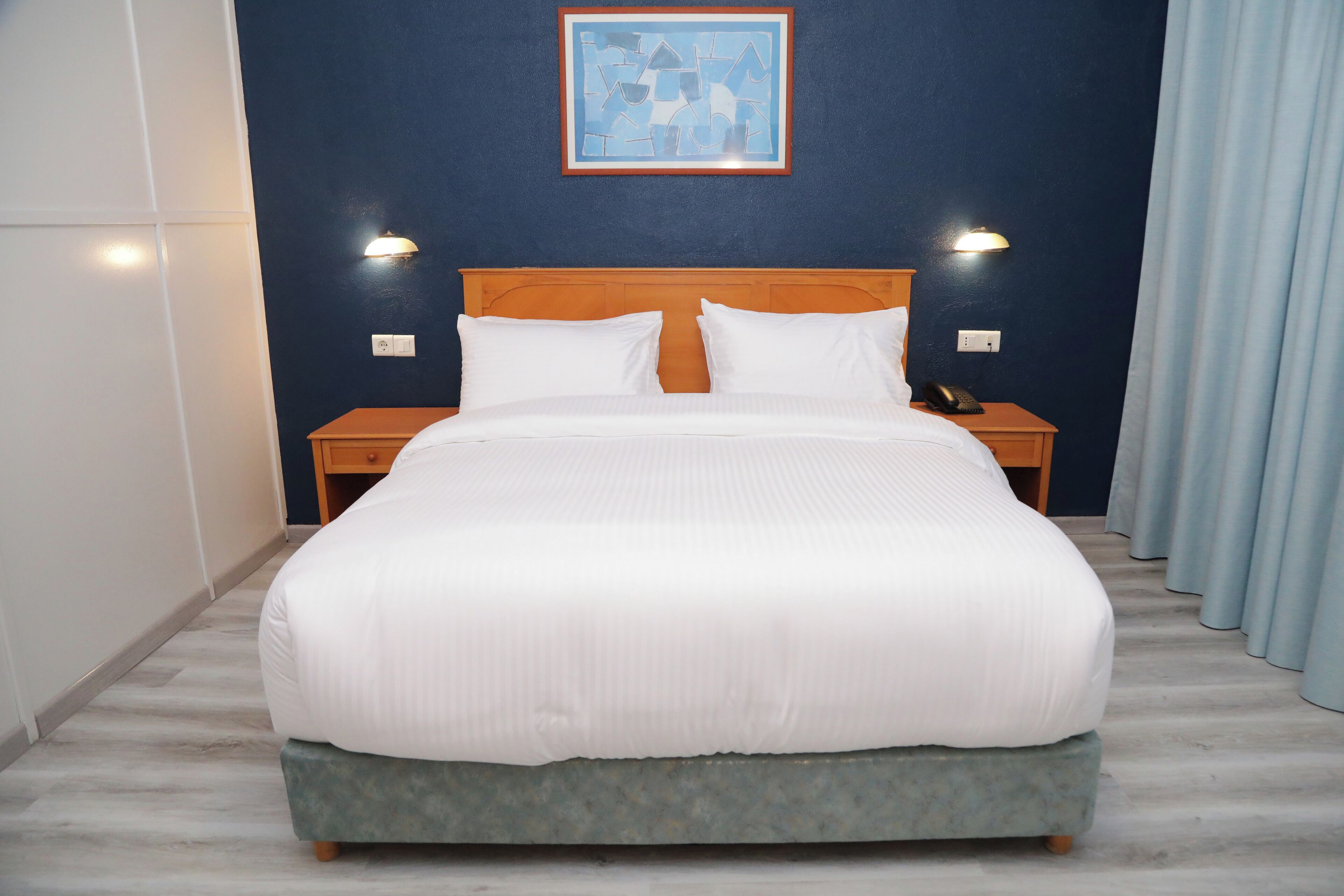 A neatly made bed with white linens, a wooden headboard, and two bedside lamps.