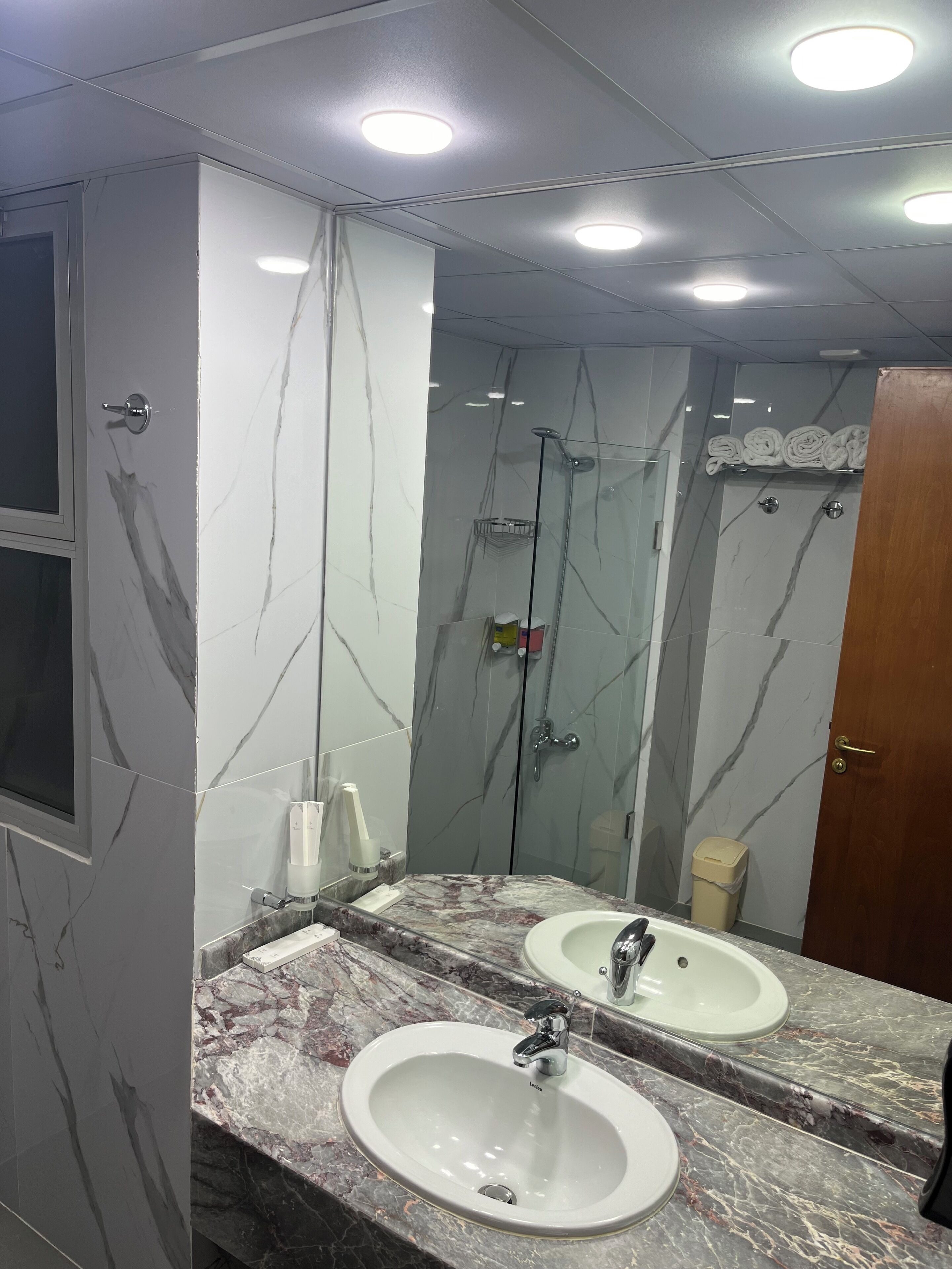 A bathroom with marble walls, two sinks, a shower, and a mirror.