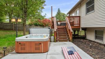 Een achtertuin met een jacuzzi, een houten terras, een trap en een huis.