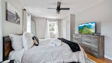 A bedroom with a bed, a ceiling fan, a TV, a dresser, and a window.
