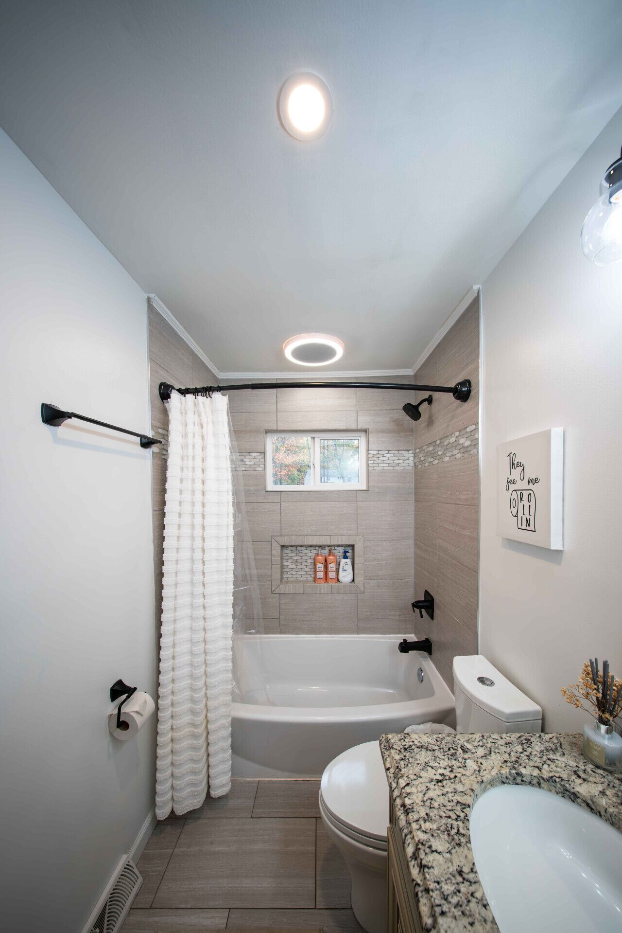 A modern bathroom with a freestanding bathtub, a toilet, and a sink with a granite countertop.