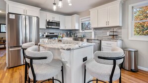 Cocina moderna con armarios blancos, electrodomésticos de acero inoxidable, una isla central con taburetes y luminarias colgantes.