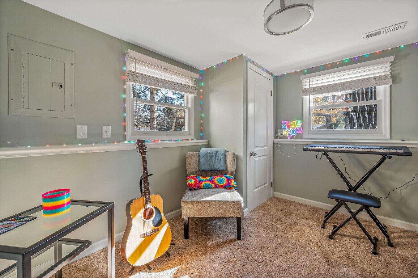 A room with a guitar, a keyboard, and a chair with a colorful cushion.