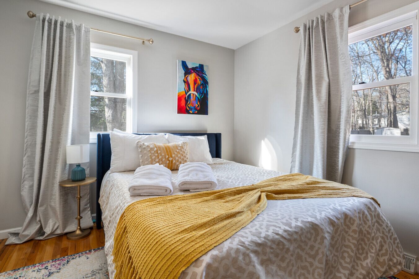 Una camera da letto ordinata con un letto, cuscini, una coperta e un quadro appeso al muro.