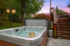 Ein Whirlpool mit zwei Sektgläsern, umgeben von Bäumen und einer Holzterrasse.