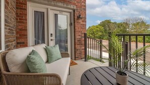 Een balkon met een rieten bank, een potplant en een deur met daarop '102'.