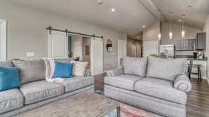 Ein geräumiges Wohnzimmer mit zwei grauen Sofas, einem Couchtisch und einer Küche im Hintergrund.