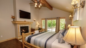 Un dormitorio con cama de madera, chimenea, televisor y un ventanal con vistas a zonas verdes.