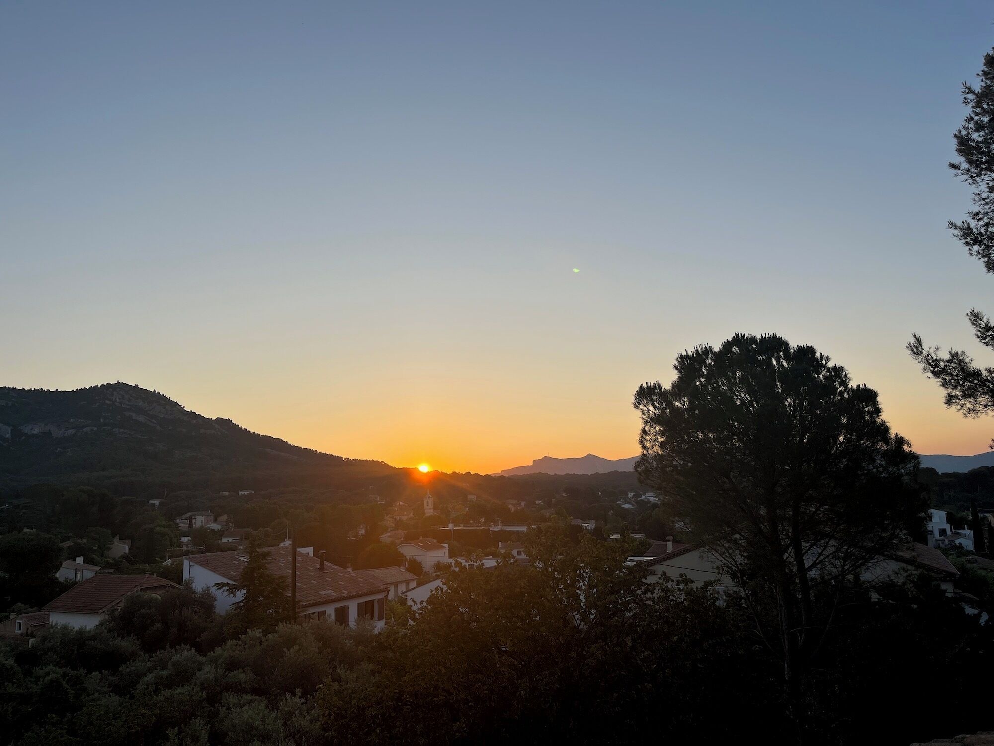 A sunset over a town with buildings and hills in the background.