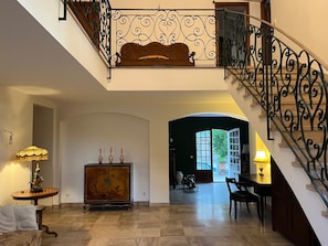 Un hall d’entrée spacieux avec un grand escalier, un meuble en bois orné d’objets décoratifs et une vue sur la pièce adjacente.