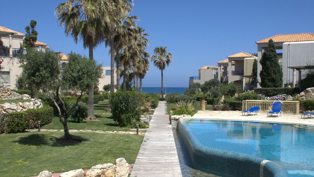 A wooden pathway leading to a swimming pool with a clear view of the ocean and palm trees. - 1 Bedroom Apartment on Beach Elias Upper (Platanias)