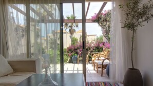 A room with a sofa, a table with a vase, a colorful rug, a potted plant, and a view of an outdoor patio with chairs and flowers. - 1 Bedroom Apartment on Beach Elias Upper (Platanias)
