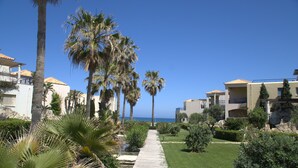 A pathway lined with palm trees leading to a building with a tiled roof. - 1 Bedroom Apartment on Beach Elias Upper (Platanias)
