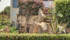A garden with rocks, a chair, and a building with a window. - 1 Bedroom Apartment on Beach Elias Upper (Platanias)