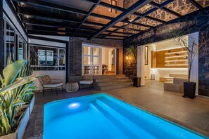 A modern indoor pool area with a stone wall, seating, and a staircase leading to a bar area. - Espigal 2 · Mansión de lujo Alto Palmas-5Hab Piscina y Jacuzzi (Envigado)