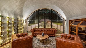 Un rincón de descanso acogedor con sofás de cuero, una mesa de centro redonda y una estantería con botellas de vino.