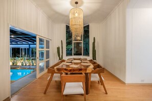 A dining area with a wooden table, white chairs, and a hanging light fixture. - Espigal 2 · Mansión de lujo Alto Palmas-5Hab Piscina y Jacuzzi (Envigado)