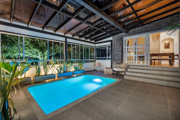 An indoor swimming pool with a view of the outdoors, surrounded by plants and seating areas. - Espigal 2 · Mansión de lujo Alto Palmas-5Hab Piscina y Jacuzzi (Envigado)