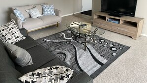 Una sala de estar con sofá, mesa de centro, mueble para televisión y una mesa con cubierta de vidrio.