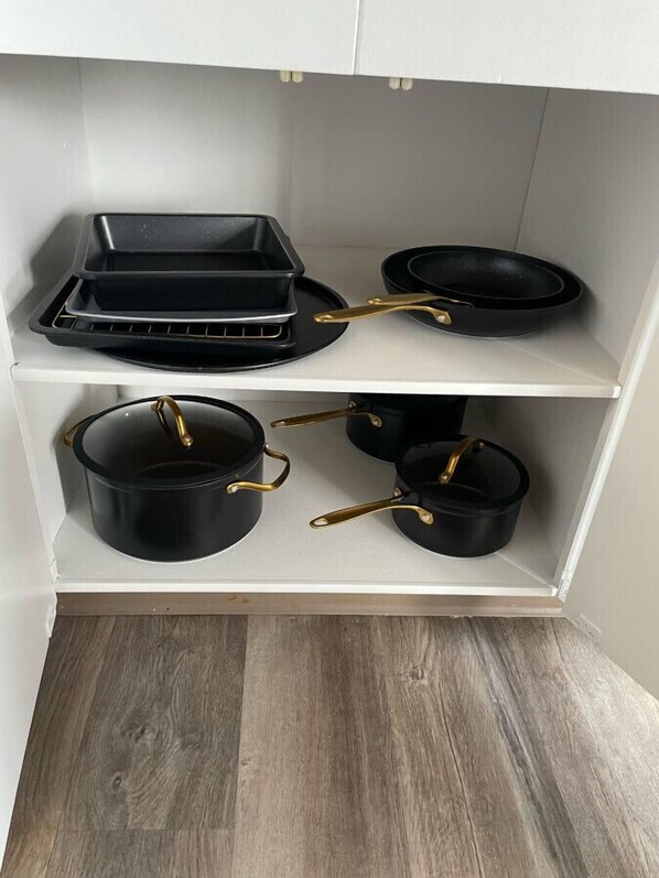 A kitchen with white cabinets and a wooden floor. There are three black pots with gold handles on the lower shelf. - Exquisite 2 Bedroom Apartment (Camrose)
