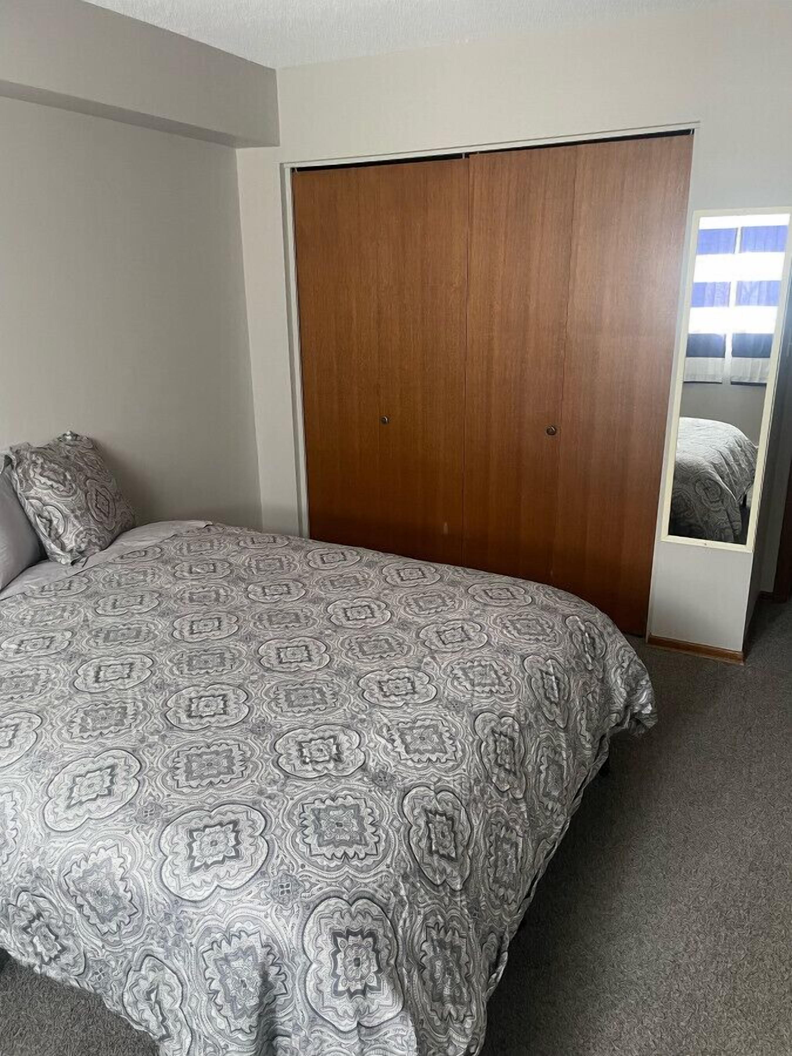 A bedroom with a bed, a wooden wardrobe, and a window with curtains.