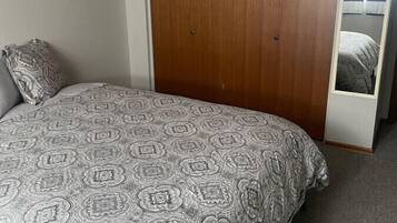 A bedroom with a bed, a wooden wardrobe, and a window with curtains.