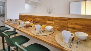 A modern kitchen with a wooden countertop, bar stools, and breakfast items like coffee cups, bowls, and fruit.