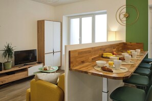Una cocina moderna con encimera de madera, zona de comedor con sillas verdes y un televisor sobre un mueble de madera.