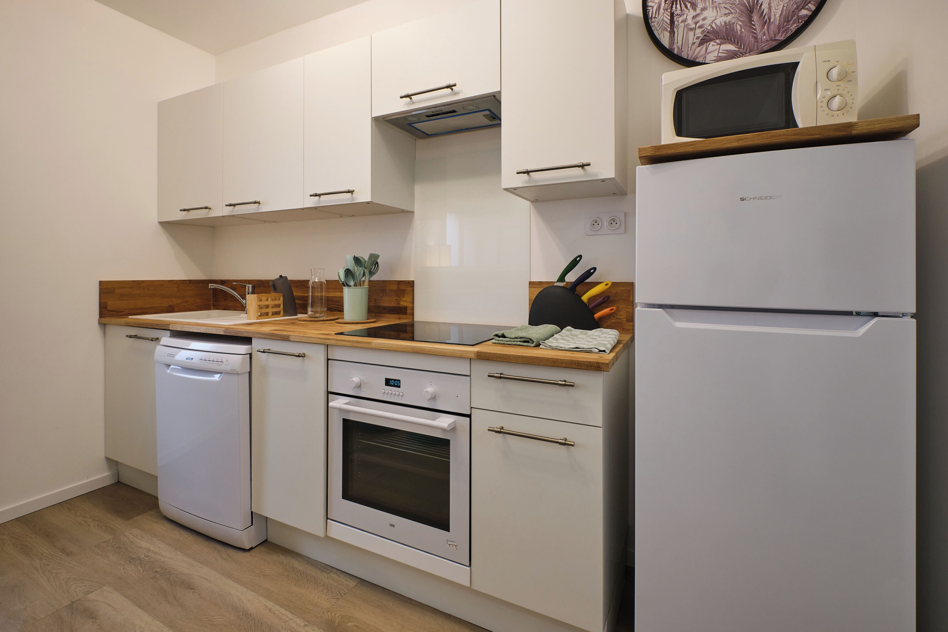 A compact kitchen with a dishwasher, oven, microwave, and a refrigerator.