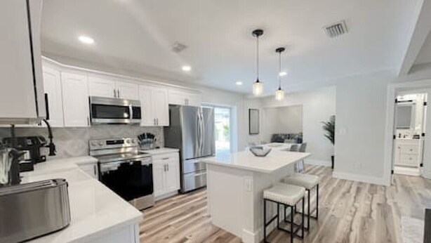 A modern kitchen with white cabinetry, stainless steel appliances, a central island with stools, and a wooden floor.