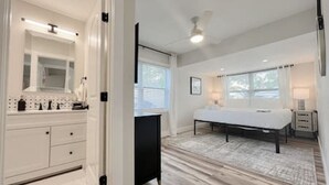 A modern bedroom with a large bed, a vanity with a mirror, and a window with blinds.