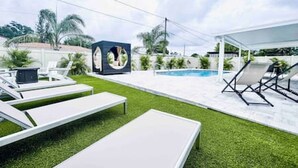 A modern outdoor pool area with lounge chairs and a covered seating area.