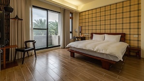 Habitación de hotel con una cama grande, un escritorio con silla, una ventana con cortinas y papel tapiz escocés.