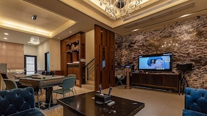 Una sala de estar moderna con mesa de billar, sofás azules, una araña, un televisor de pantalla plana grande y una pared de piedra.