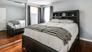 Een moderne slaapkamer met een groot bed, een donker houten hoofdbord, een nachtkastje, een spiegel en een garderobe.