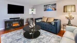 Een moderne woonkamer met een flatscreen televisie, een open haard, een blauwe bank en een decoratieve lamp.