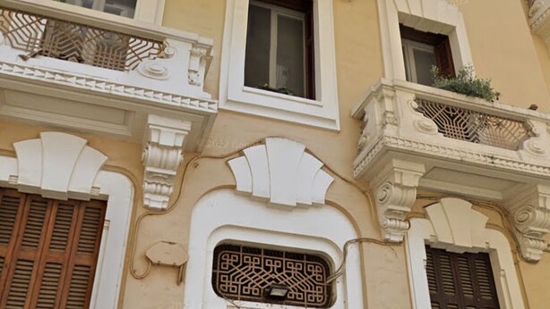 Un edificio con detalles arquitectónicos ornamentales, incluyendo balcones decorativos y una puerta de madera destacada.