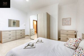 Ein Hotelzimmer mit einem Bett, zwei Nachttischen, einem Kleiderschrank, einem Spiegel und einer Tür zu einem anderen Raum.