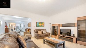 A modern living room with a leather sofa, a wooden coffee table, a TV, and a dining area in the background. - Tower Road seafront home, with 3BR & Working Space (Sliema)