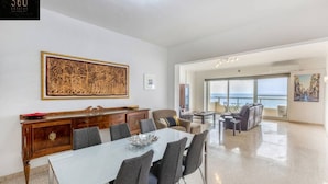 A spacious living area with a dining table, chairs, and a large window offering a view of the sea. - Tower Road seafront home, with 3BR & Working Space (Sliema)