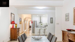 A modern dining area with a glass-top table, grey upholstered chairs, and a wooden cabinet with a red bowl on top. - Tower Road seafront home, with 3BR & Working Space (Sliema)