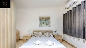 A bedroom with a large bed, two bedside tables, a wall-mounted air conditioner, and a painting. - Tower Road seafront home, with 3BR & Working Space (Sliema)