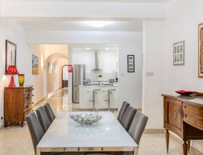 A modern dining area with a glass-top table, grey upholstered chairs, and a wooden cabinet with a red bowl on top.