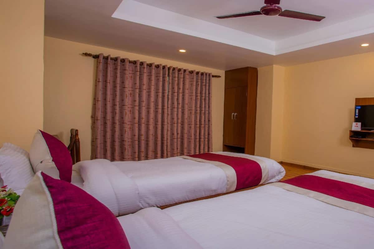 Habitación de hotel con dos camas, un ventilador de techo, un televisor montado en la pared y un ventanal con cortinas.