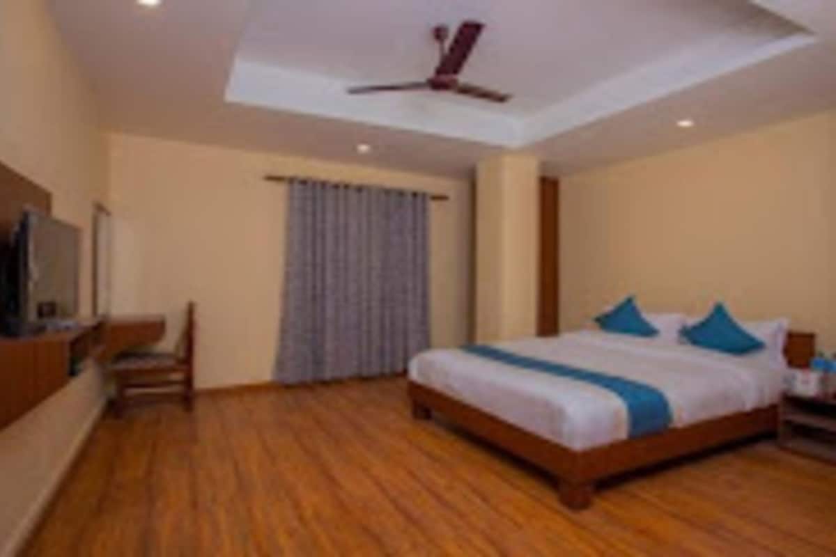 Un dormitorio con suelo de madera, una cama con almohadas azules, un ventilador de techo y un televisor sobre un mueble.