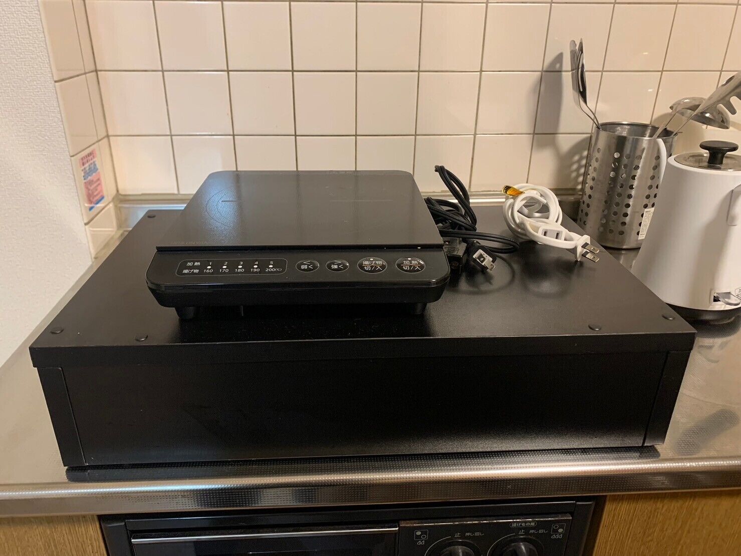 Una cocina con encimera negra, hervidor blanco y un rallador.